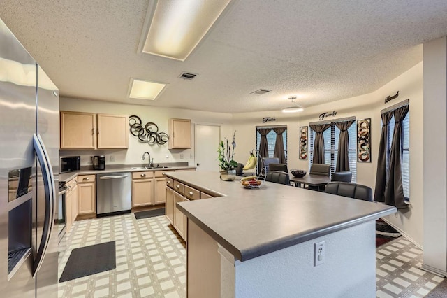 15300 Iola Cv, Austin, TX 78717 - kitchen featuring appliances with stainless steel finishes, light flooring, light brown cabinets, a sink, and a center island