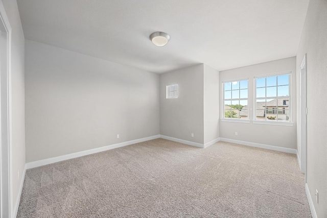 spare room featuring light colored carpet and baseboards