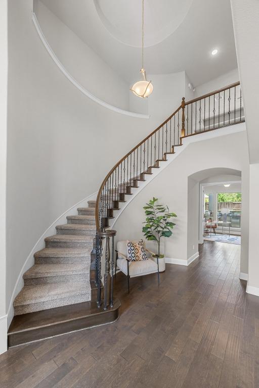 stairway with arched walkways, wood finished floors, a towering ceiling, baseboards, and recessed lighting
