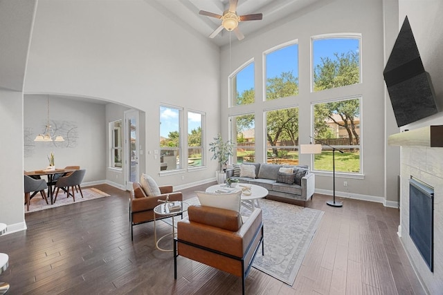 living area with a tile fireplace, arched walkways, ceiling fan, baseboards, and dark wood-type flooring