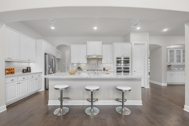 kitchen featuring arched walkways, backsplash, stainless steel appliances, white cabinetry, and recessed lighting