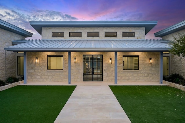 1785 Backbone Rdg, Wimberley, TX 78666 - back of house at dusk featuring a standing seam roof, metal roof, a lawn, and a patio area