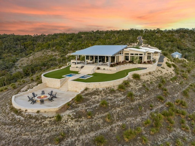 1785 Backbone Rdg, Wimberley, TX 78666 - back of property at dusk with an outdoor fire pit, a patio, an outdoor pool, and a wooded view