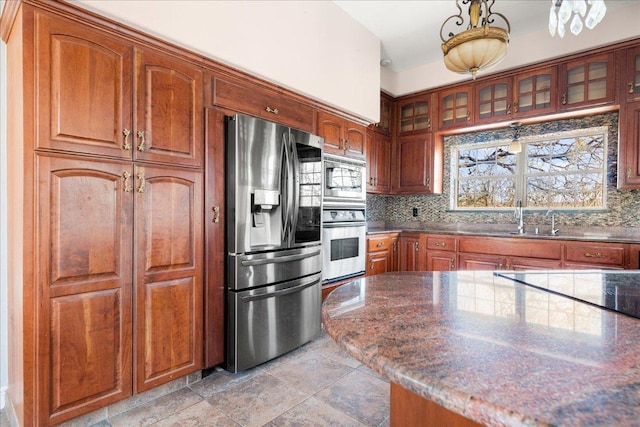 2604 Saratoga Dr, Austin, TX 78733 - kitchen featuring stainless steel appliances, decorative backsplash, glass insert cabinets, and brown cabinets