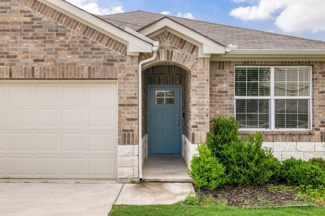 entrance to property with a garage, brick siding, driveway, and roof with shingles