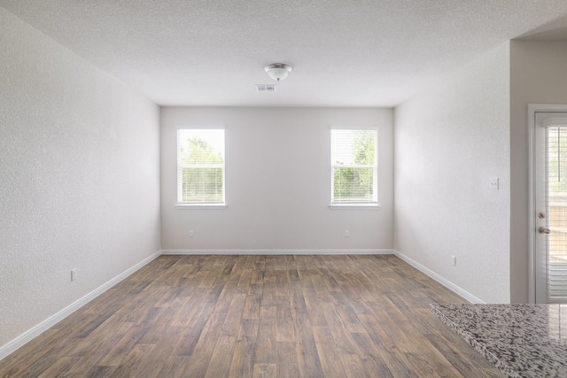 empty room with dark wood-type flooring, baseboards, and a textured wall