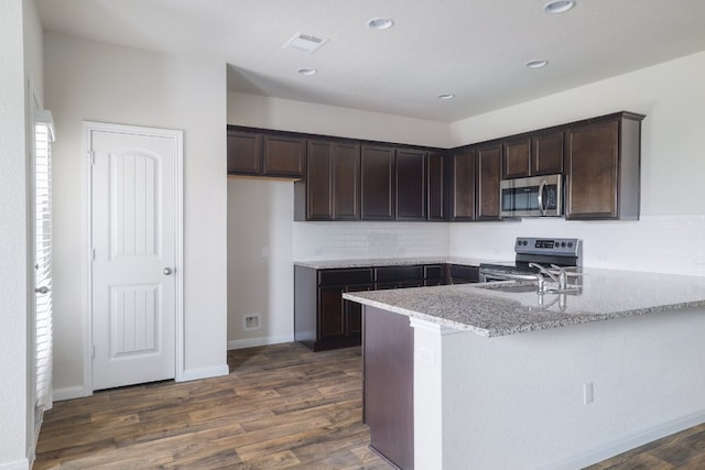 kitchen with appliances with stainless steel finishes, dark brown cabinetry, dark wood-style flooring, and recessed lighting