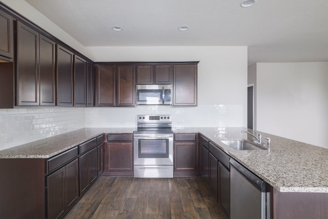 kitchen with stainless steel appliances, a sink, a peninsula, dark wood finished floors, and light stone countertops