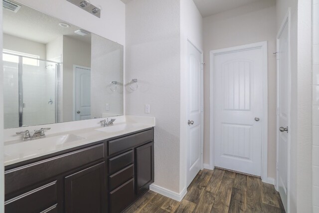 full bathroom with wood finished floors, a stall shower, double vanity, and baseboards