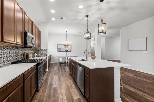 kitchen featuring appliances with stainless steel finishes, a sink, dark wood-style flooring, baseboards, and backsplash