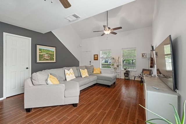 living area with a ceiling fan, dark wood-type flooring, and a towering ceiling