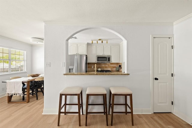 2812 Sissinghurst Dr, Austin, TX 78745 - kitchen featuring appliances with stainless steel finishes, arched walkways, a kitchen bar, light wood finished floors, and ornamental molding
