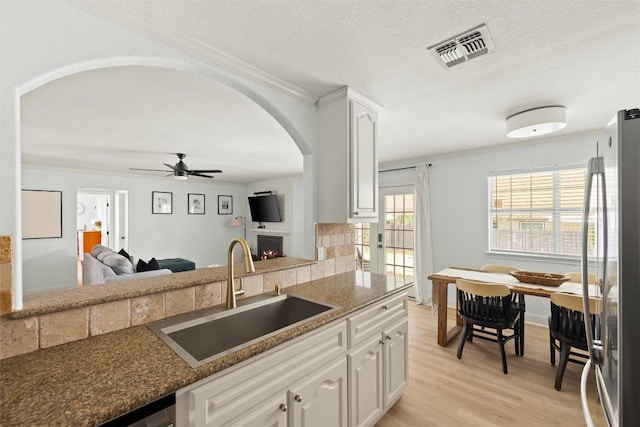 2812 Sissinghurst Dr, Austin, TX 78745 - kitchen featuring a sink, arched walkways, freestanding refrigerator, a ceiling fan, and a lit fireplace