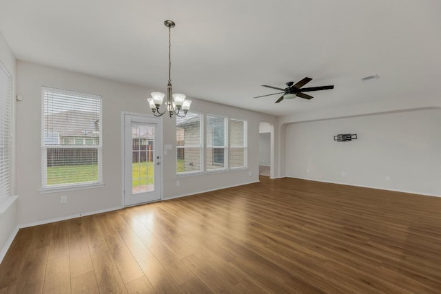 unfurnished dining area featuring a ceiling fan, wood finished floors, a chandelier, baseboards, and arched walkways