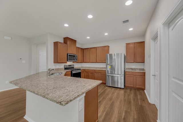 kitchen with appliances with stainless steel finishes, a sink, wood finished floors, a peninsula, and brown cabinets