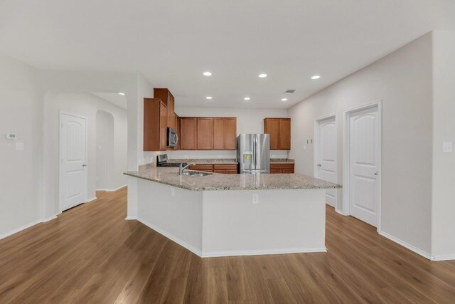 kitchen with stainless steel appliances, wood finished floors, a peninsula, brown cabinets, and light stone countertops