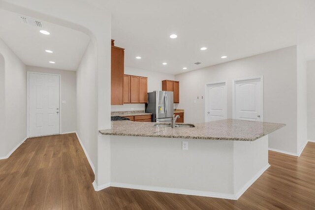kitchen featuring stainless steel refrigerator with ice dispenser, brown cabinetry, wood finished floors, a sink, and baseboards