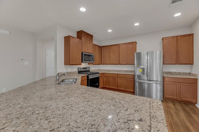 kitchen featuring stainless steel appliances, a sink, light stone counters, brown cabinets, and recessed lighting