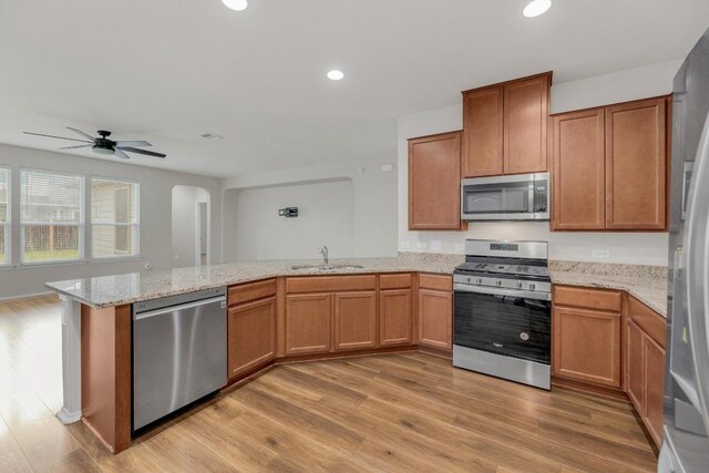 kitchen with appliances with stainless steel finishes, a sink, a peninsula, arched walkways, and a ceiling fan