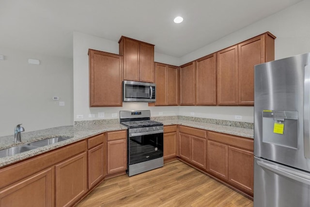 kitchen with stainless steel appliances, a sink, light wood-style flooring, light stone counters, and brown cabinets