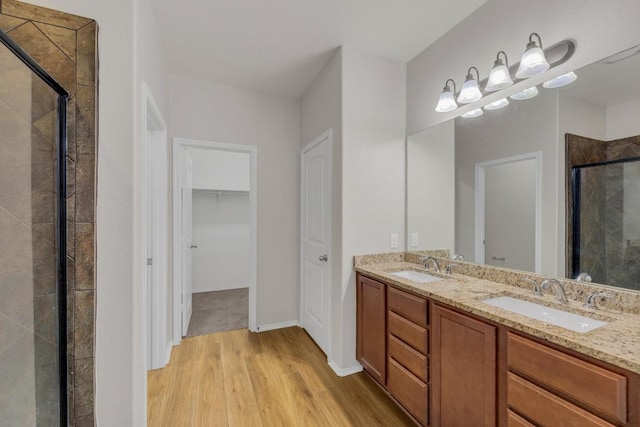full bath featuring wood finished floors, a stall shower, double vanity, a walk in closet, and baseboards
