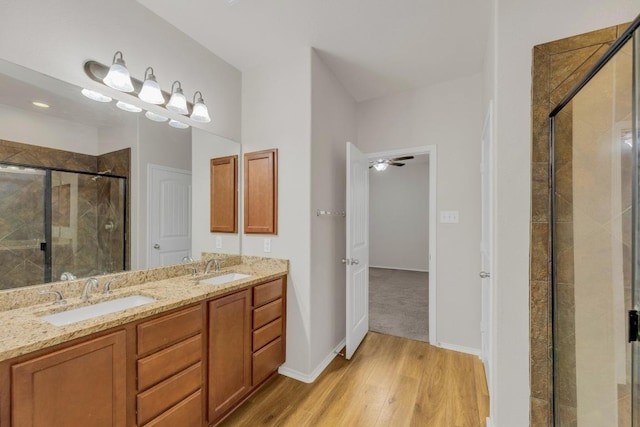full bathroom featuring a shower stall, wood finished floors, double vanity, and baseboards