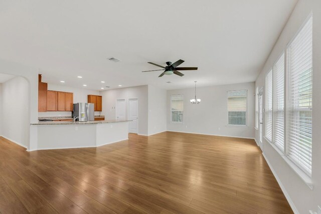 unfurnished living room with a ceiling fan, wood finished floors, a chandelier, recessed lighting, and baseboards