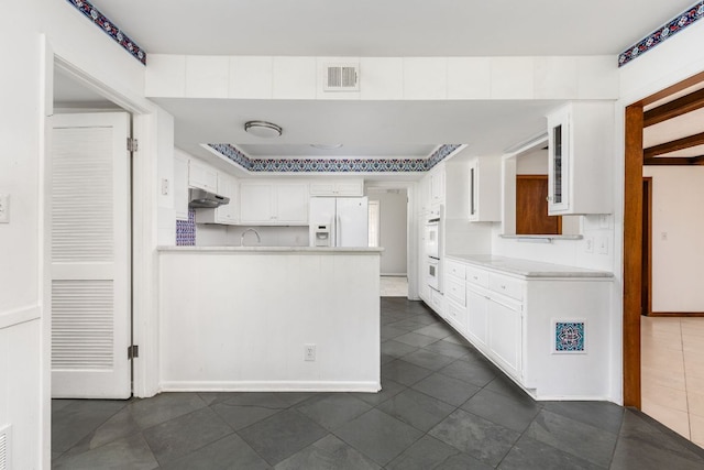 4007 Edgerock Dr, Austin, TX 78731 - kitchen featuring white appliances, a peninsula, dark tile patterned flooring, white cabinetry, and light countertops