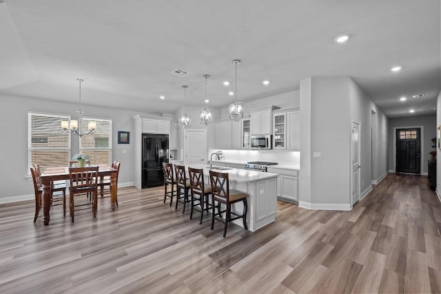 kitchen with appliances with stainless steel finishes, a chandelier, light countertops, a kitchen bar, and a center island with sink