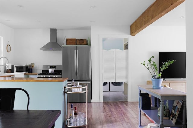 4906 Hilldale Dr, Austin, TX 78723 - kitchen with appliances with stainless steel finishes, wall chimney exhaust hood, separate washer and dryer, wood counters, and wood finished floors