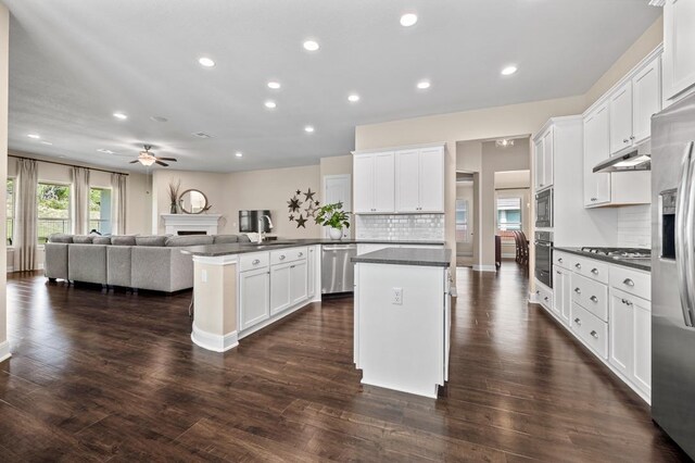 kitchen with stainless steel appliances, dark countertops, a peninsula, open floor plan, and a fireplace