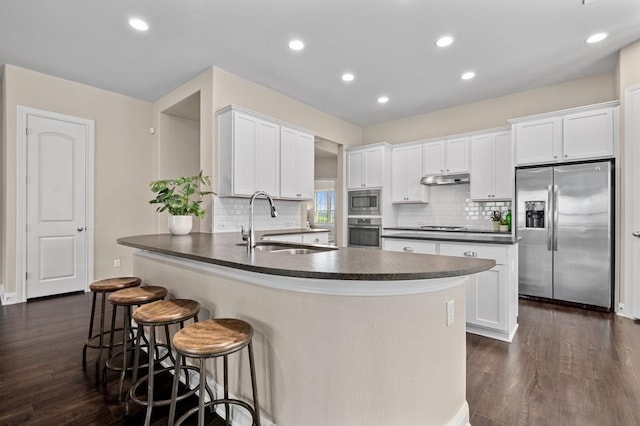 kitchen featuring stainless steel appliances, a sink, dark countertops, a peninsula, and under cabinet range hood