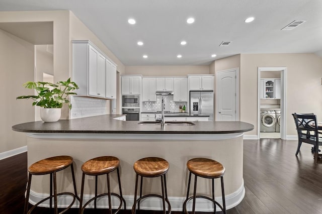 kitchen with appliances with stainless steel finishes, dark countertops, washing machine and dryer, dark wood-type flooring, and recessed lighting