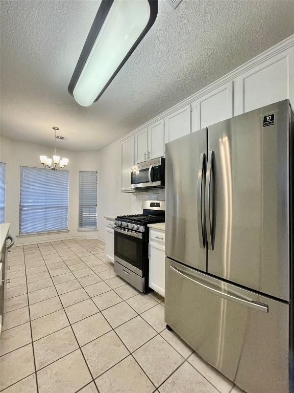 1816 Lancaster St, San Marcos, TX 78666 - kitchen with stainless steel appliances, white cabinetry, light tile patterned floors, a chandelier, and a textured ceiling