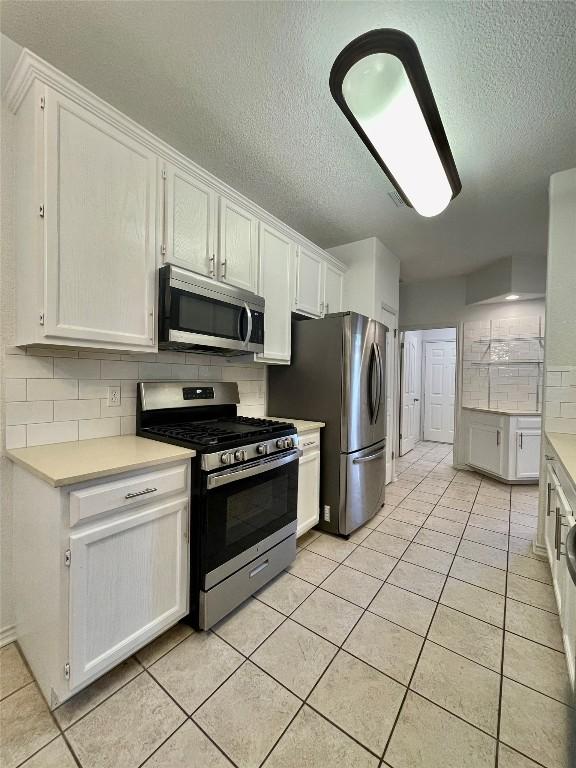 1816 Lancaster St, San Marcos, TX 78666 - kitchen with appliances with stainless steel finishes, a textured ceiling, white cabinetry, light countertops, and backsplash
