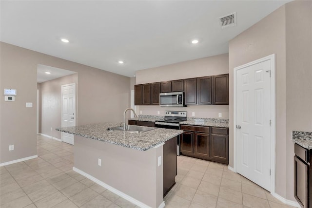 625 Taggart Trl, Jarrell, TX 76537 - kitchen featuring appliances with stainless steel finishes, light tile patterned floors, dark brown cabinets, a sink, and a center island with sink