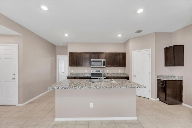 625 Taggart Trl, Jarrell, TX 76537 - kitchen featuring appliances with stainless steel finishes, dark brown cabinets, baseboards, an island with sink, and light stone countertops