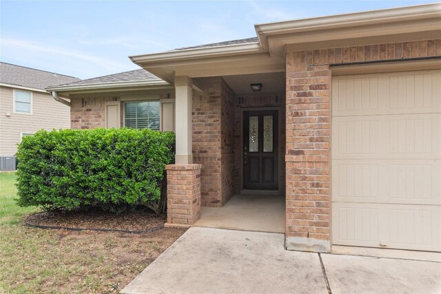 property entrance featuring brick siding, a garage, and a shingled roof