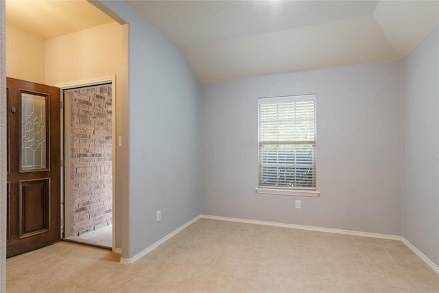 unfurnished room with lofted ceiling, light tile patterned flooring, and baseboards