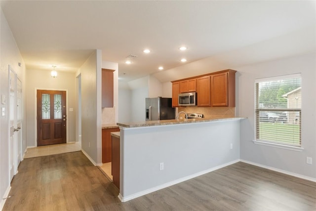 kitchen with appliances with stainless steel finishes, brown cabinets, light wood-type flooring, backsplash, and recessed lighting
