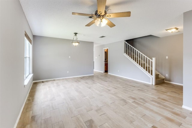unfurnished living room featuring stairs, ceiling fan, light wood-style flooring, and baseboards