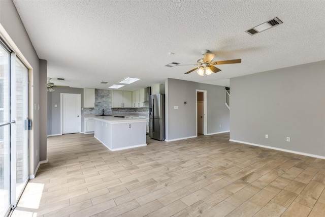 kitchen featuring stainless steel refrigerator with ice dispenser, a ceiling fan, open floor plan, light countertops, and a textured ceiling