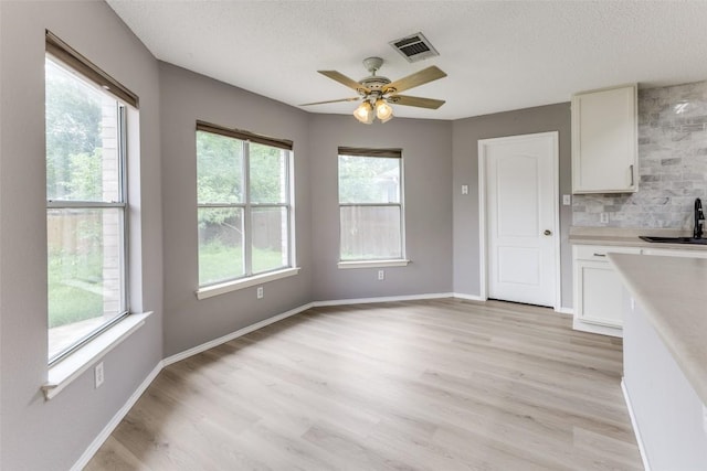 unfurnished dining area with ceiling fan, light wood-style flooring, a textured ceiling, a sink, and baseboards