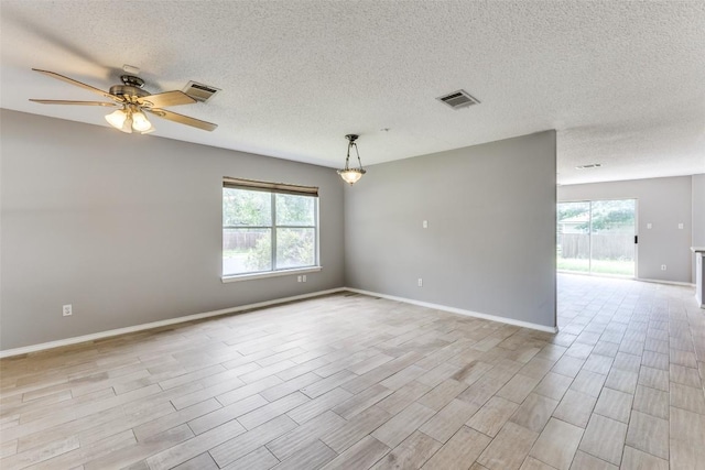 empty room with plenty of natural light, a ceiling fan, a textured ceiling, and light wood-style floors