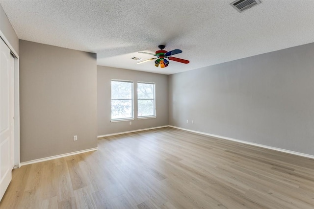 spare room featuring ceiling fan, light wood-style floors, a textured ceiling, and baseboards