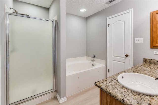 bathroom featuring a stall shower, a bath, wood finished floors, a textured ceiling, and vanity
