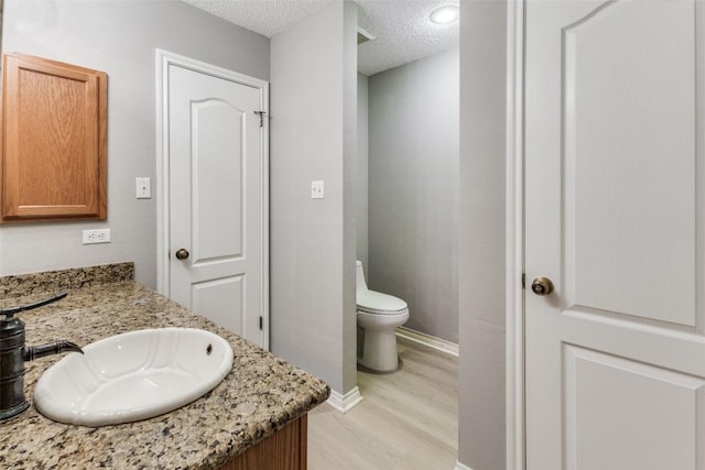 bathroom featuring wood finished floors, toilet, a textured ceiling, baseboards, and vanity