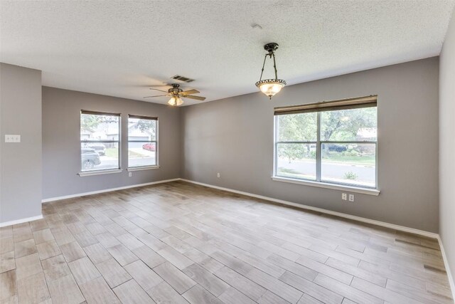 empty room with healthy amount of natural light, ceiling fan, a textured ceiling, baseboards, and wood finished floors