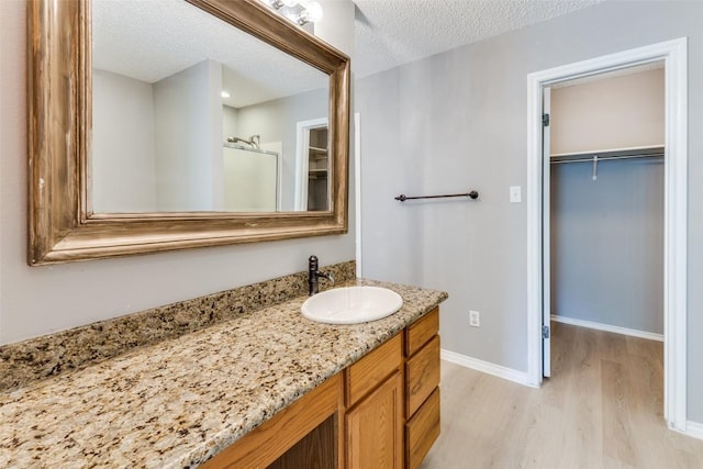 bathroom with wood finished floors, a walk in closet, vanity, a stall shower, and a textured ceiling