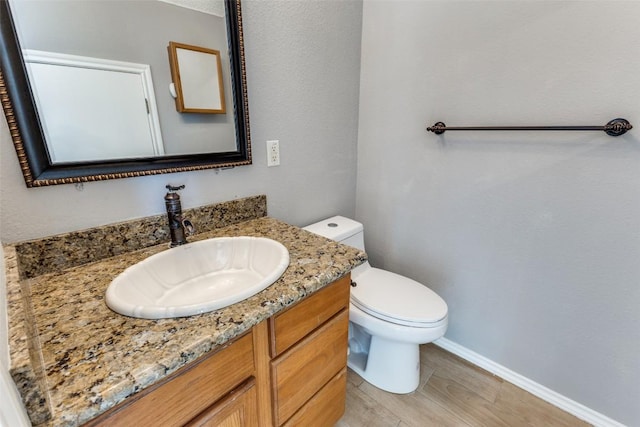 half bathroom featuring vanity, baseboards, wood finished floors, and toilet